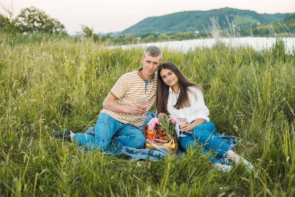 young happy couple having picnic outdoors in the countryside during beautiful sunset. Romantic date near the lake - Photo, Image