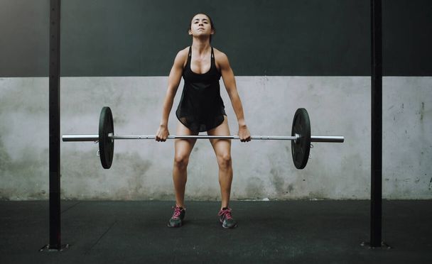 With a little effort you can build ultimate power. a young woman exercising with a barbell in a gym - Photo, Image