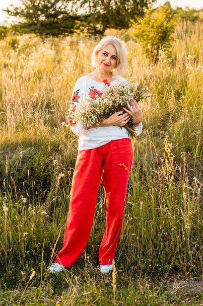 portrait of happy joyfull mature woman with a bouquet of wildflowers in countryside during beautiful sunset - Photo, Image