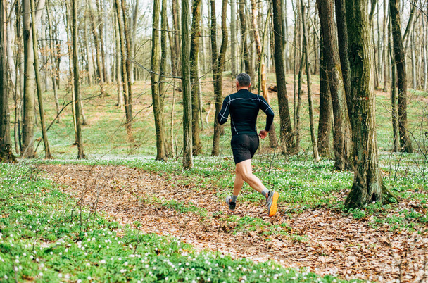 wide shot of sporty man running in beautiful spring forest. Sport and wellness concept - Foto, imagen