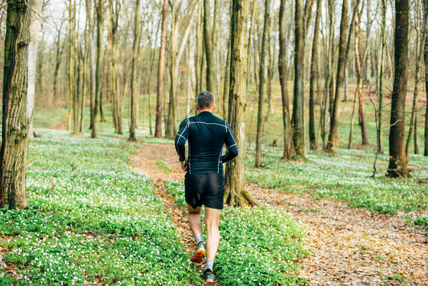 wide shot of sporty man running in beautiful spring forest. Sport and wellness concept - Foto, Imagem
