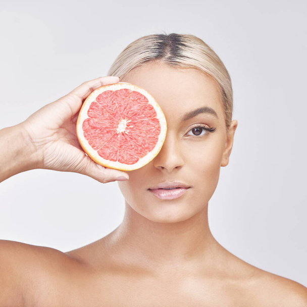 Een citrus uitzicht. Studio shot van een mooie jonge vrouw met een grapefruit voor haar ogen tegen een grijze achtergrond - Foto, afbeelding