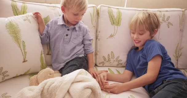 Ξανθό αγόρι γαργαλάει τα πόδια του αδελφού του σε έναν καναπέ - Πλάνα, βίντεο