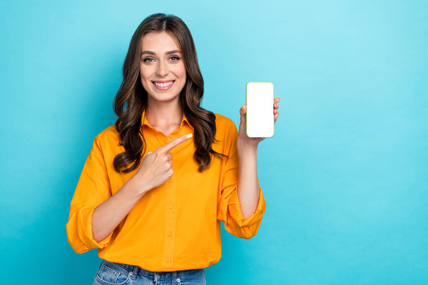 Photo of cheerful pretty person indicate finger empty space telephone display isolated on blue color background. - Foto, afbeelding