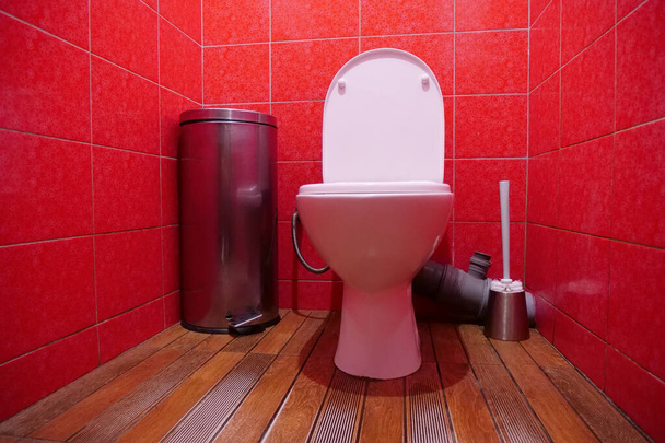 Интерьер туалетной комнаты с белой унитазом с открытой крышкой, металлической мусорной корзиной, туалетной щеткой и красной стеновой плиткой - Фото, изображение