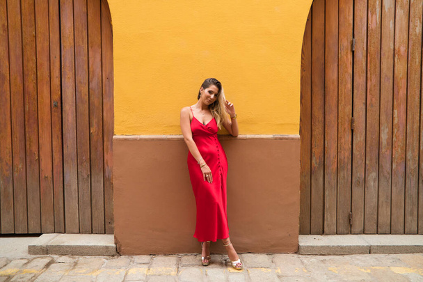 Young, blonde, beautiful woman in a red dress is visiting seville. The woman poses for the camera very elegant and like a model in the typical streets of the city. Holidays and travels - Fotoğraf, Görsel