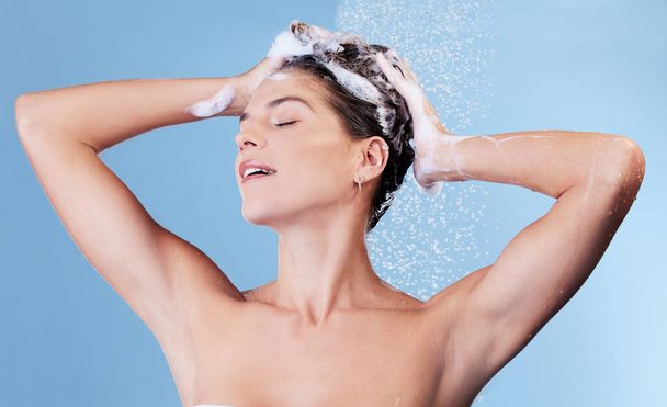 Es gibt nichts Erfrischenderes als dieses quietschsaubere Gefühl. Studioaufnahme einer jungen Frau, die sich beim Duschen vor blauem Hintergrund die Haare mit Shampoo wäscht - Foto, Bild