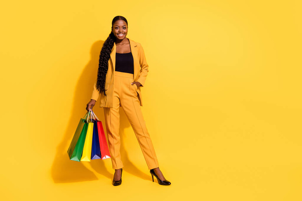 Full length photo of nice young lady stand with bags wear suit high heels isolated on yellow background. - Фото, зображення