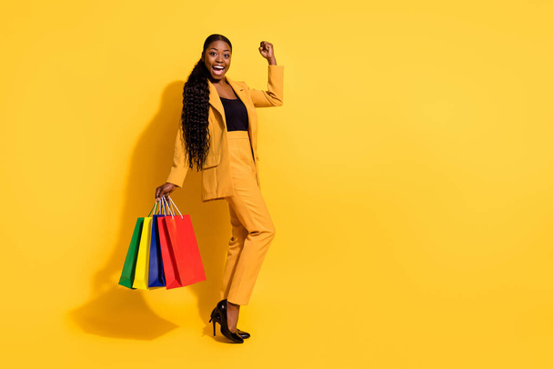Full body photo of hooray young lady yell with bags wear jacket pants high heels isolated on yellow background. - Zdjęcie, obraz