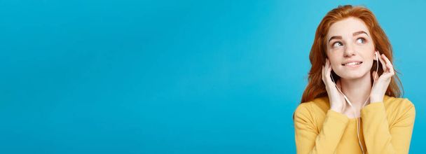 Lifestyle concept - Портрет веселой жизнерадостной рыжеволосой девушки с имбирными волосами, которая любит слушать музыку в наушниках и радостно улыбается камере. Изолирован на фоне Blue Pastel. Копирование пространства
 - Фото, изображение