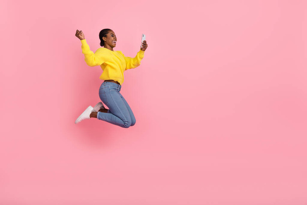 Full body profil boczny zdjęcie młodej dziewczyny skoczek wygląd mobilny świętować triumf pięści ręka odizolowane na różowy kolor tła. - Zdjęcie, obraz