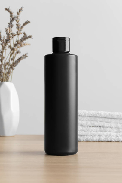 Black cosmetic lotion bottle mockup with a lavender and towels on the wooden table. - 写真・画像