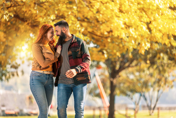 Giovane coppia felice che si guarda mentre si tiene per mano e cammina nel parco autunnale. - Foto, immagini