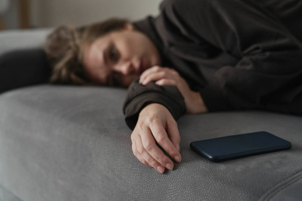 Λευκή γυναίκα με διανοητικό πρόβλημα ξαπλωμένη με κινητό στον καναπέ. - Φωτογραφία, εικόνα
