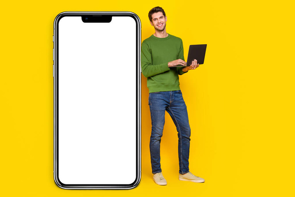 Photo of attractive cute young guy wear green sweater working modern device empty space isolated yellow color background. - Photo, image