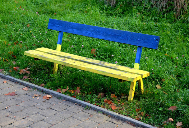 un banco del parque hecho de madera está parado en el borde de la acera. está pintado en colores nacionales ucranianos. en lugar de banderas, la gente pinta bancos y muebles en la plaza. bandera - Foto, imagen