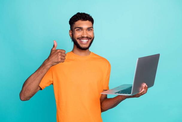 Portrait of cheerful handsome guy hold netbook hand finger demonstrate thumb up feedback isolated on teal color background. - Foto, Imagen