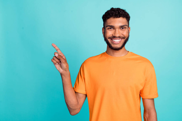 Photo of sweet good mood man dressed orange t-shirt pointing finger empty space isolated turquoise color background. - Photo, image