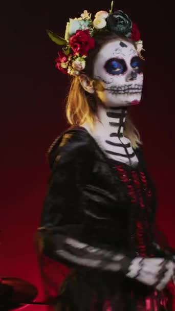 Pionowe wideo: Przerażająca pani śmierci z makijażem czaszki i kostiumem horroru, aby uczcić dios de los muertos na meksykańskim halloween. Przerażająca kobieta przebrana za Mikołaja Muerte w dzień martwego święta. - Materiał filmowy, wideo