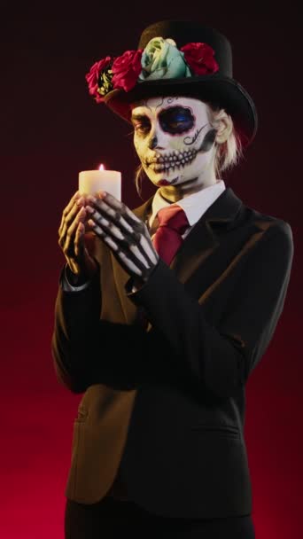 Vertical video: Woman with skull make up blowing burning candle in studio, being dressed as goddess of death to celebrate dios de los muertos. Putting out flame and acting creepy on traditional - Footage, Video