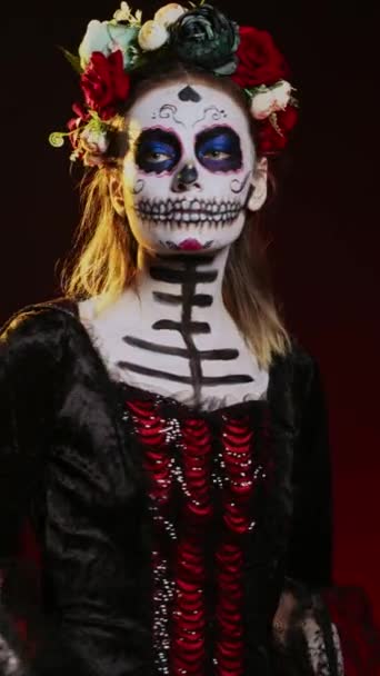 Vídeo vertical: Hermosa dama de muerto posando en traje de halloween con cráneo maquillarse para celebrar dios de los muertos en fiesta mexicana. Mujer espeluznante como santa muerte con arte corporal en blanco y negro - Metraje, vídeo