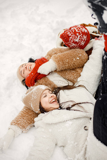 Joyful teens and their beautiful mother spending time together in the winter park. Family lay on a snow. Family wearing warm jackets and knitted hats. - Foto, Imagen
