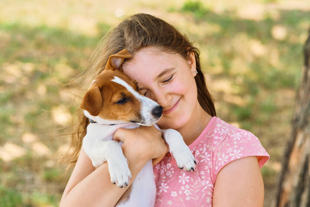 A menina tem um filhote nos braços. Miúdo bonito abraçando Jack Russel cachorro terrier no parque de verão. O conceito de amizade, cuidado, infância feliz. - Foto, Imagem