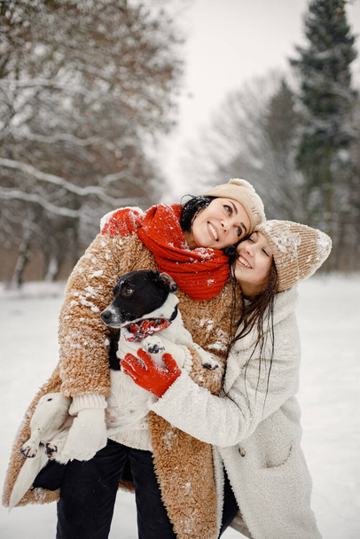 Joyful girl and her beautiful mother spending time together in the winter park. Woman wearing warm jacket and red sweater. Family having fun and hugging. - Zdjęcie, obraz