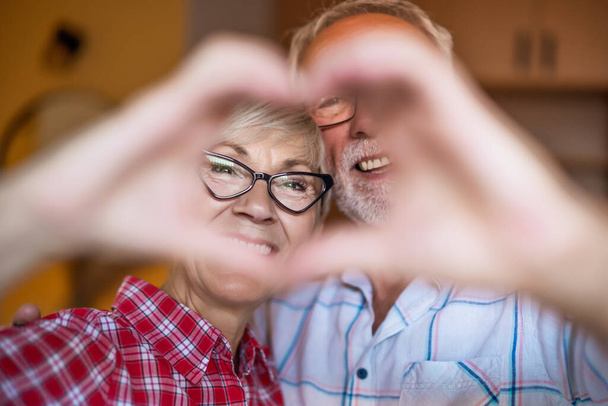 Happy senior couple is embracing and making heart shape with their hands. - Φωτογραφία, εικόνα