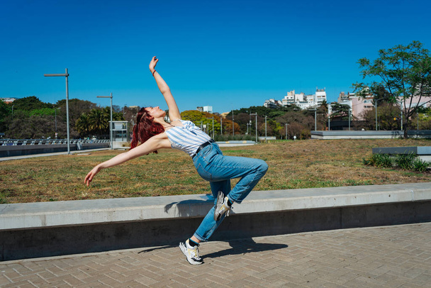 Hermosa joven latina bailando felizmente en la calle mientras festeja con saltos y volteretas. Concepto de alegría, danza callejera, hip hop, juventud. - Foto, Imagen