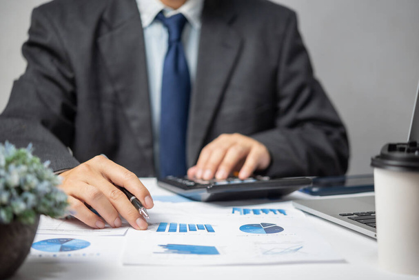 Businessman hand pointing paperwork chart report analysis statistic and document financial graph with computer laptop at office.Business investment marketing on desk in company. - Foto, Imagem