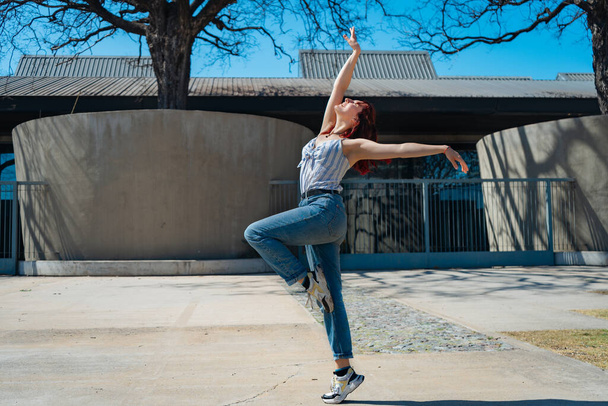 Красивая молодая латиноамериканка счастливо танцует на улице, веселясь с прыжками и сальто. Радость, уличные танцы, хип-хоп, молодость. - Фото, изображение
