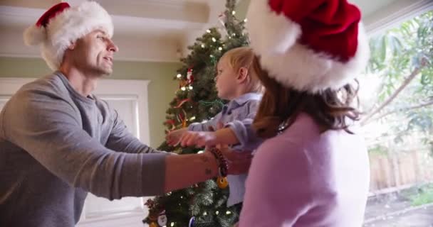 Gut aussehende Eltern und entzückende zwei Kinder, die einen Weihnachtsbaum betrachten - Filmmaterial, Video