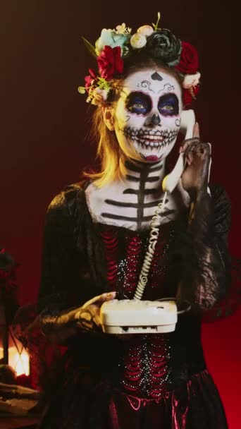 Вертикальное видео: модель Goddess, использующая стационарный телефон для ответа на звонок, держащая в руках телефон на празднике Fican dios de los muertos. Выглядит как Кавалера Катрина, празднующая день мертвых. - Кадры, видео