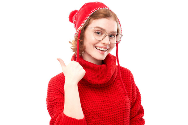 Portré pozitív vörös hajú fiatal nő piros karácsonyi pulóver mosolygós ujjal mutogatva üres másolási hely szöveg vagy termék elszigetelt fehér háttér, reklám banner - Fotó, kép