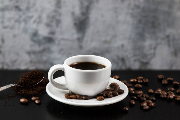 Bodegón con taza blanca con deliciosos granos de café y café sobre fondo oscuro - Foto, imagen