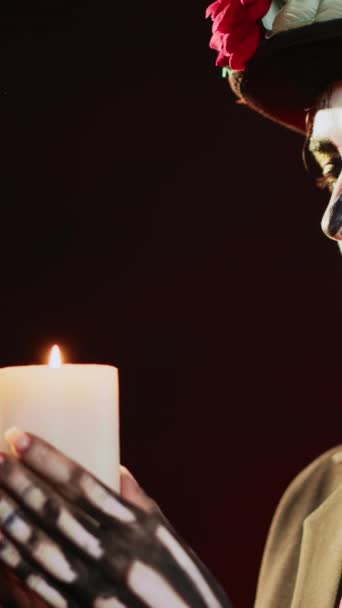 Вертикальное видео: Женщина-модель в роли Санта-муэрте, задувающая свечу в студии, потушающая пламя огня и носящая костюм кавалеры-катрины. Празднование дня умершего мексиканского Хэллоуина. Портативный - Кадры, видео