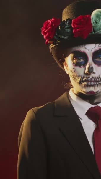 Vertikální video: Strašidelná bohyně v halloweenském kostýmu s lebkou tvoří oslavu svaté mexické tradice, pózování ve studiu. Vypadá to jako dáma smrti na obřadní oslavě Santa Muerte. Handheld - Záběry, video