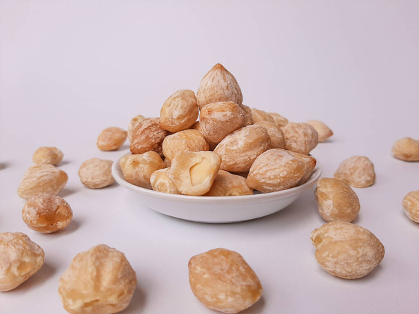 Αλευρίτες moluccanus ή Ινδονησίας Candlenuts ονομάζεται Kemiri, μέσα σε ένα smale πλάκα, απομονώνονται σε λευκό φόντο - Φωτογραφία, εικόνα