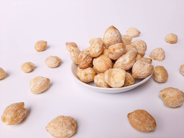Αλευρίτες moluccanus ή Ινδονησίας Candlenuts ονομάζεται Kemiri, μέσα σε ένα smale πλάκα, απομονώνονται σε λευκό φόντο - Φωτογραφία, εικόνα