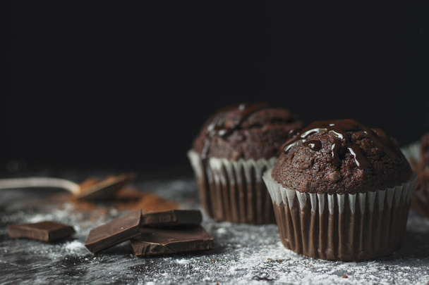 Close up van cacao muffins met chocolade glazuur op rustieke tafel bedekt met suiker en cacao met vintage lepel en lege ruimte - Foto, afbeelding