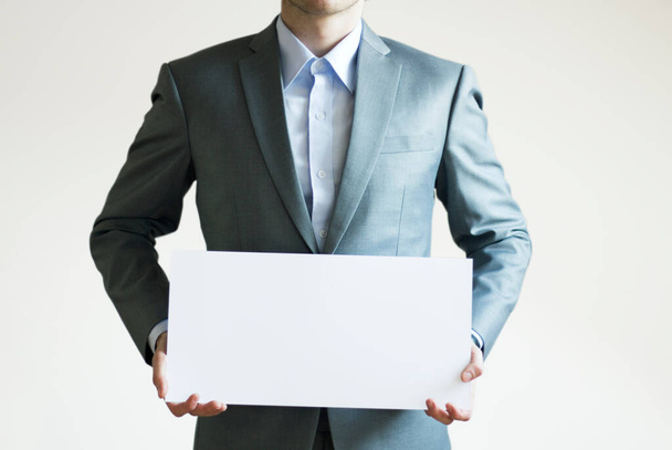 Φωτογραφία ενός επιχειρηματία με γκρι κοστούμι που κρατά οριζόντιο λευκό χαρτί - Φωτογραφία, εικόνα