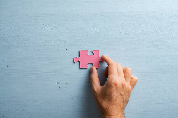 Mannelijke hand het plaatsen van een blanco roze puzzel stuk over een effen pastelblauwe houten achtergrond. - Foto, afbeelding
