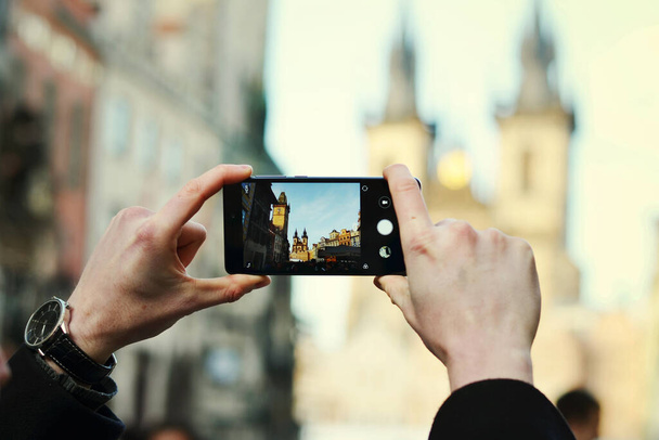 Primo piano delle mani di un uomo che tiene il telefono e fotografa l'edificio storico nel centro di Praga - Foto, immagini