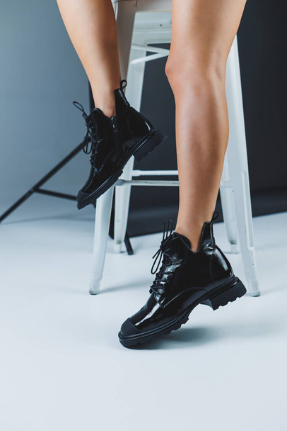 A fashionable woman stands in a store and measures autumn shoes. Close-up of female legs in stylish fashion leather black lace-up boots. New seasonal collection of women's shoes. - Foto, afbeelding