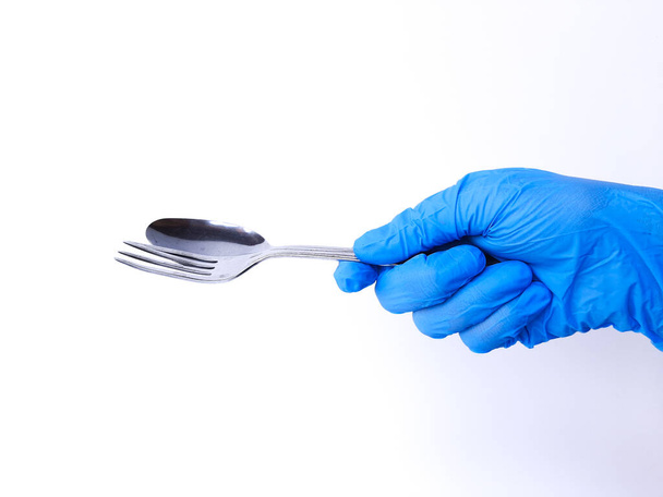 A hand with white latex glove holds metal spoon and fork. Isolated on a white background - Foto, afbeelding