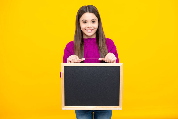 School sales board. Cheerful teenage girl kid hold blackboard chalkboard with copy space on yellow background - Photo, Image