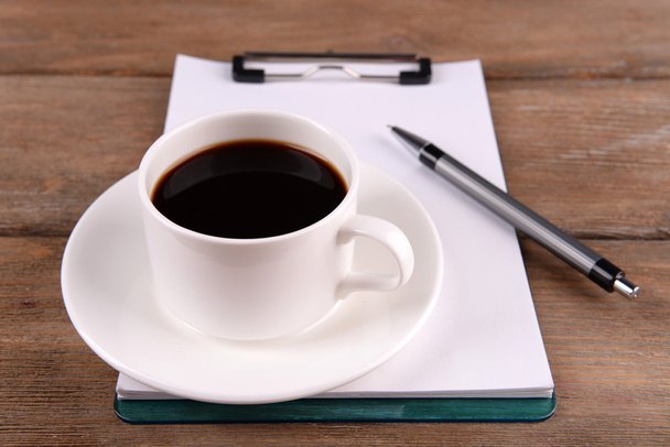 Tasse Kaffee auf Untertasse mit Blatt Papier und Stift auf Holztischhintergrund - Foto, Bild