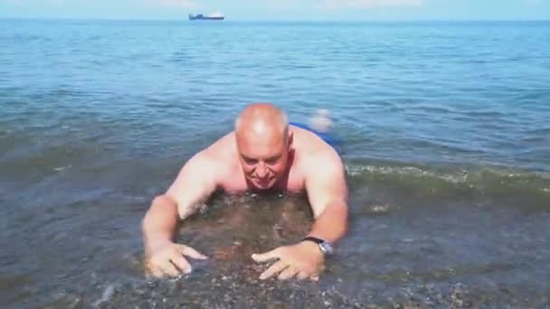 An elderly man lies on the seashore in the water. - Footage, Video