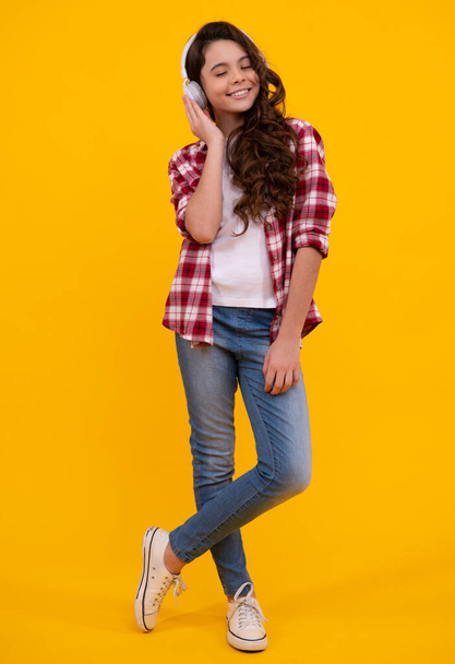 Teenager child girl in headphones listening music, wearing stylish casual outfit isolated over yellow background. Happy teenager with earphones, positive and smiling emotions of teen girl - Foto, immagini